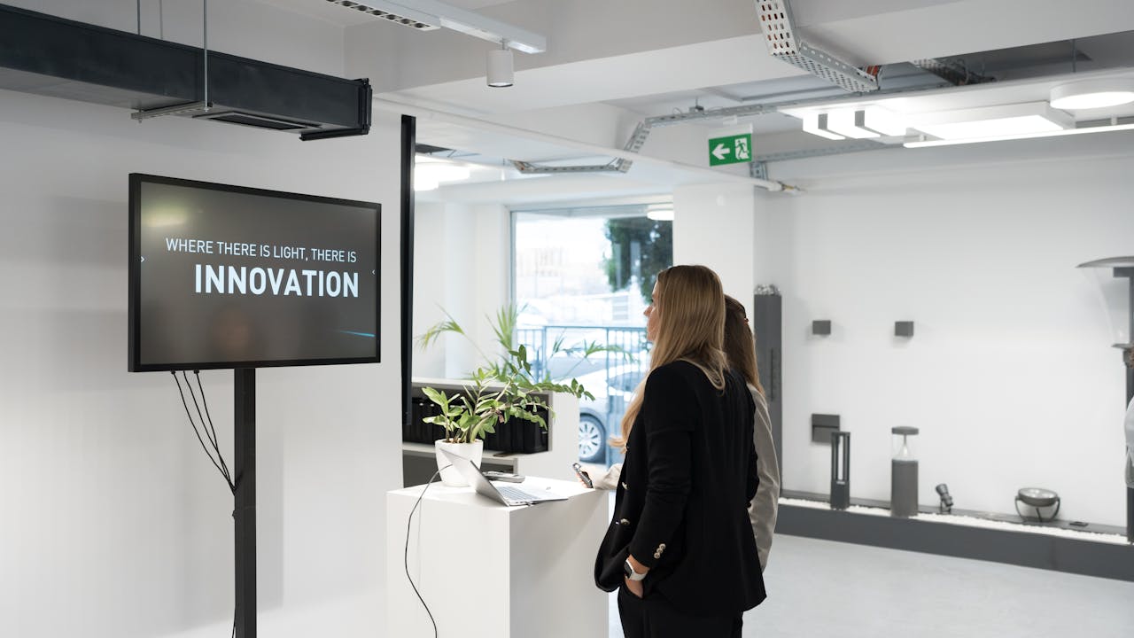 Two businesswomen discussing innovation in a modern office with a motivational screen.